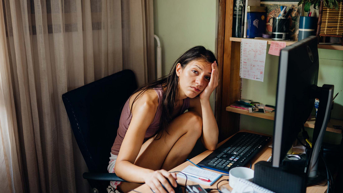 Erschöpfte Frau sitzt zu Hause vor dem Computer. 