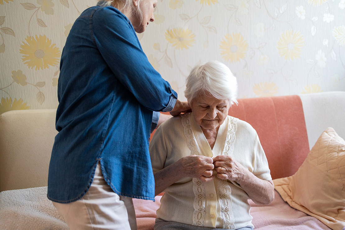 Ältere Dame erhält von Pflegerin Hilfe.