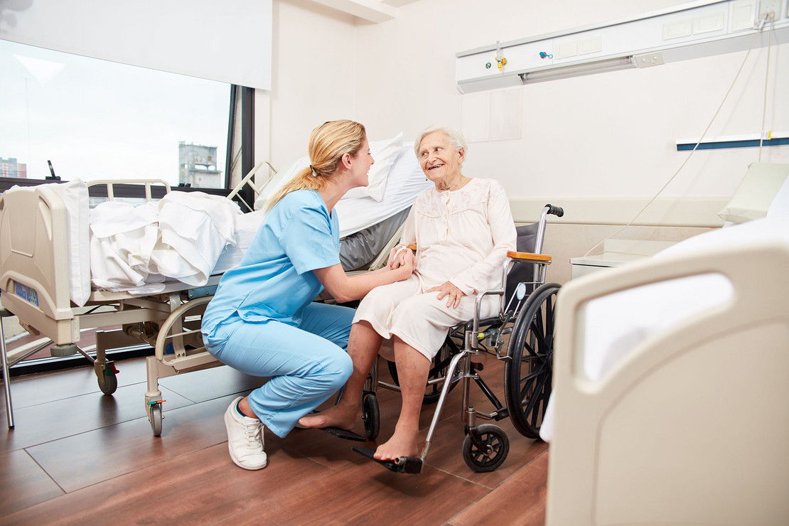 Krankenschwester mit einer Patientin im Rollstuhl im Krankenhauszimmer. 