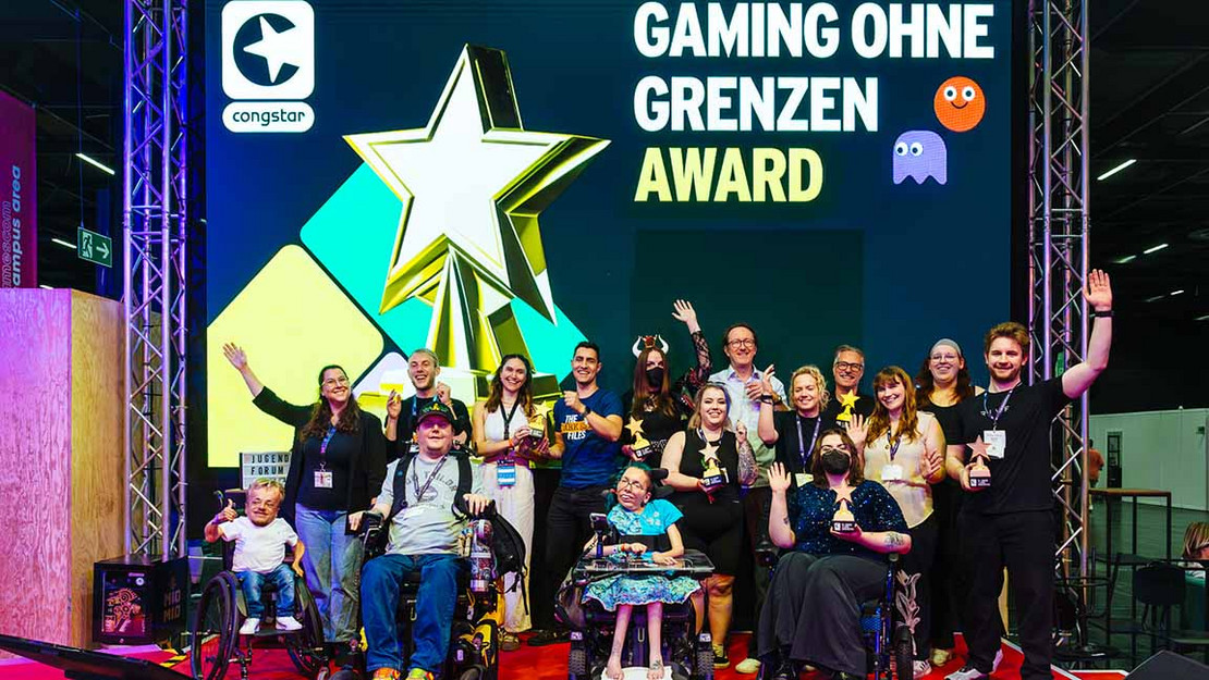 Gruppe von Menschen, viele davon im Rollstuhl auf einer Bühne. Im Hintergrund eine Leinwand mit dem text "Gaming ohne Grenzen Award"