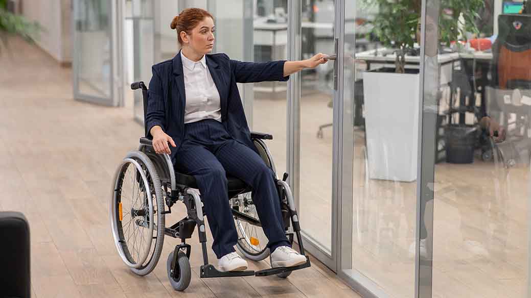 Frau im Rollstuhl an einer Glastür im Büro. 